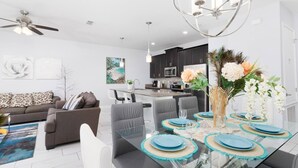 A modern kitchen with dark cabinets, a central island, and a dining area with a glass table set for six. - Storey Lake Home w/ Pool | Mins to Disney | 4BR | Waterpark (Kissimmee)