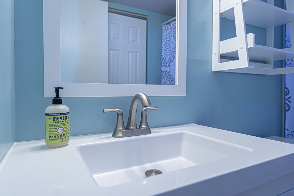 Une salle de bain avec un lavabo blanc, un miroir et un flacon de savon pour les mains.