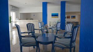 Un hall d’hôtel avec un comptoir d’accueil, des chaises à rayures bleues disposées autour d’une table centrale et des œuvres d’art accrochées aux murs.