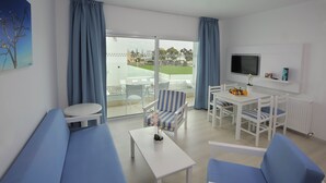 Un salon moderne comprenant un canapé, des fauteuils, une table basse et un coin repas avec un téléviseur et une étagère.