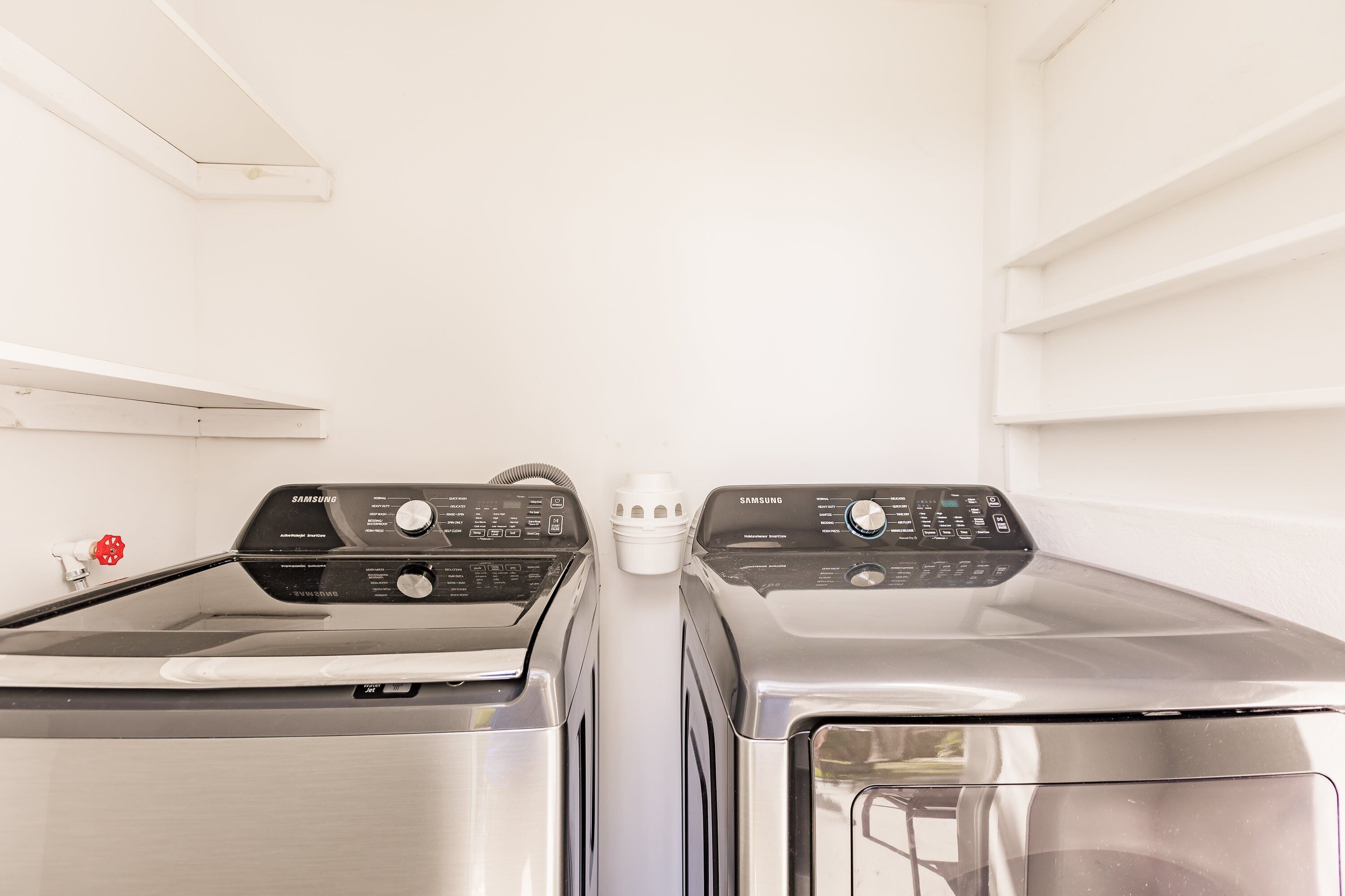 Deux machines à laver Samsung dans une buanderie aux murs et au plafond blancs.