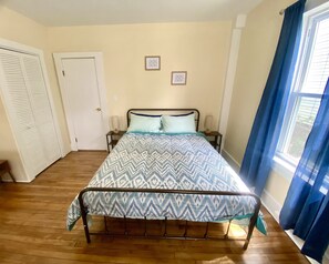 A bedroom with a bed, two bedside tables, a window with curtains, and a door.