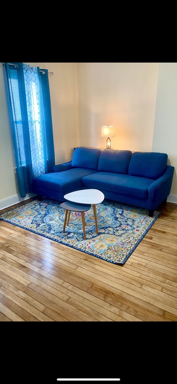 A living room with a blue sofa, a round white table, and a patterned rug on a wooden floor.