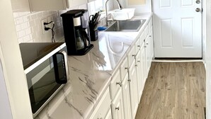A kitchen with white cabinets, a microwave, a sink, and a door. - Cozy, 2 BR APt in Worcester Close to Downtown, Palladium, DCU center, Polar Park (Worcester)