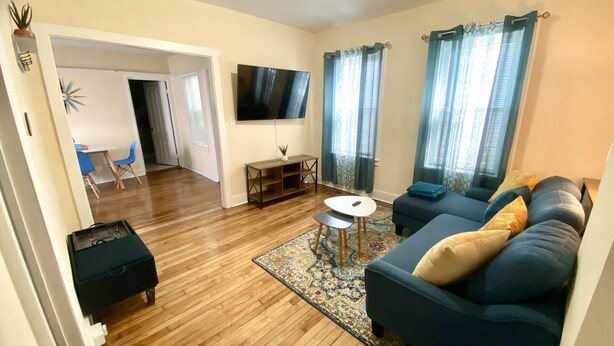 A living room with a blue sofa, a small round table, and a TV mounted on the wall. - Cozy, 2 BR APt in Worcester Close to Downtown, Palladium, DCU center, Polar Park (Worcester)