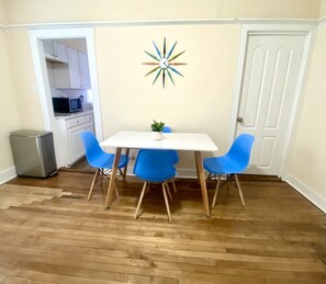 A dining area with a white table and blue chairs, a decorative clock on the wall, and a microwave in the background.