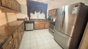Una cocina con armarios de madera, un refrigerador de acero inoxidable, lavavajillas y piso de baldosas.