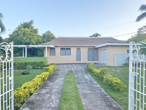 A house with a paved driveway leading to a garage, surrounded by a well-maintained lawn and yellow flowering bushes.