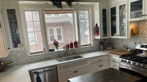 A kitchen with white cabinets, a stainless steel refrigerator, a wooden countertop, and a stove. - The Brickmason’s House (Racine)