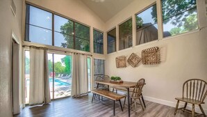 Un comedor con una mesa de madera, sillas y un banco. Amplias ventanas ofrecen luz natural y vistas al exterior.