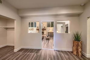 A hallway with a wooden floor, a closet, and a view into a living area with a fireplace.