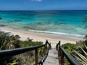 Een houten trap die naar een strand leidt, met helder turquoise water en een zandstrand.
