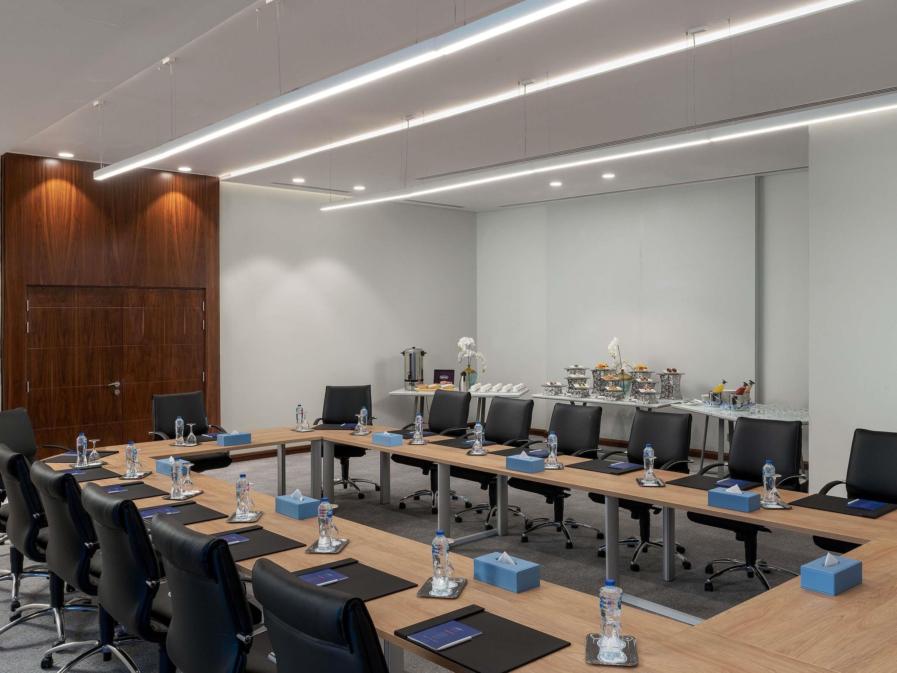 A conference room with long tables, chairs, water bottles, tissues, and decorative items.