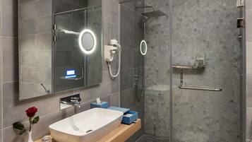 Un baño moderno con cabina de ducha de vidrio, tocador con espejo grande y una rosa en la encimera.
