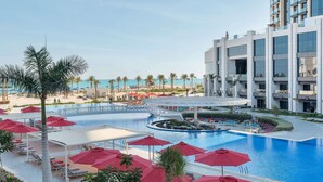 A resort pool area with umbrellas, lounge chairs, and a view of the beach and ocean. - Rixos Premium Alamein (El Alamein)