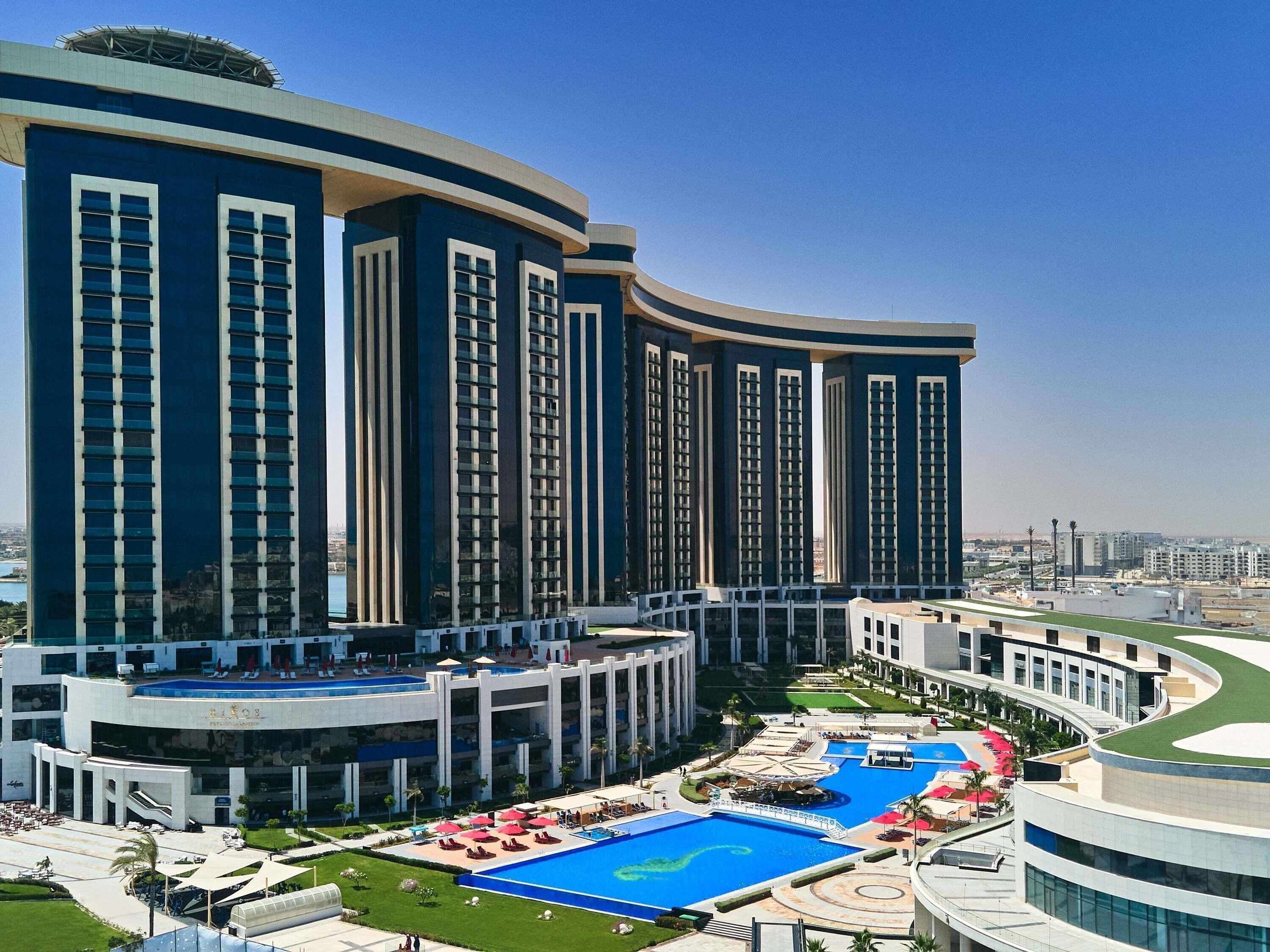 Un hotel moderno con un amplio área de piscina, varios balcones y vistas a la ciudad.