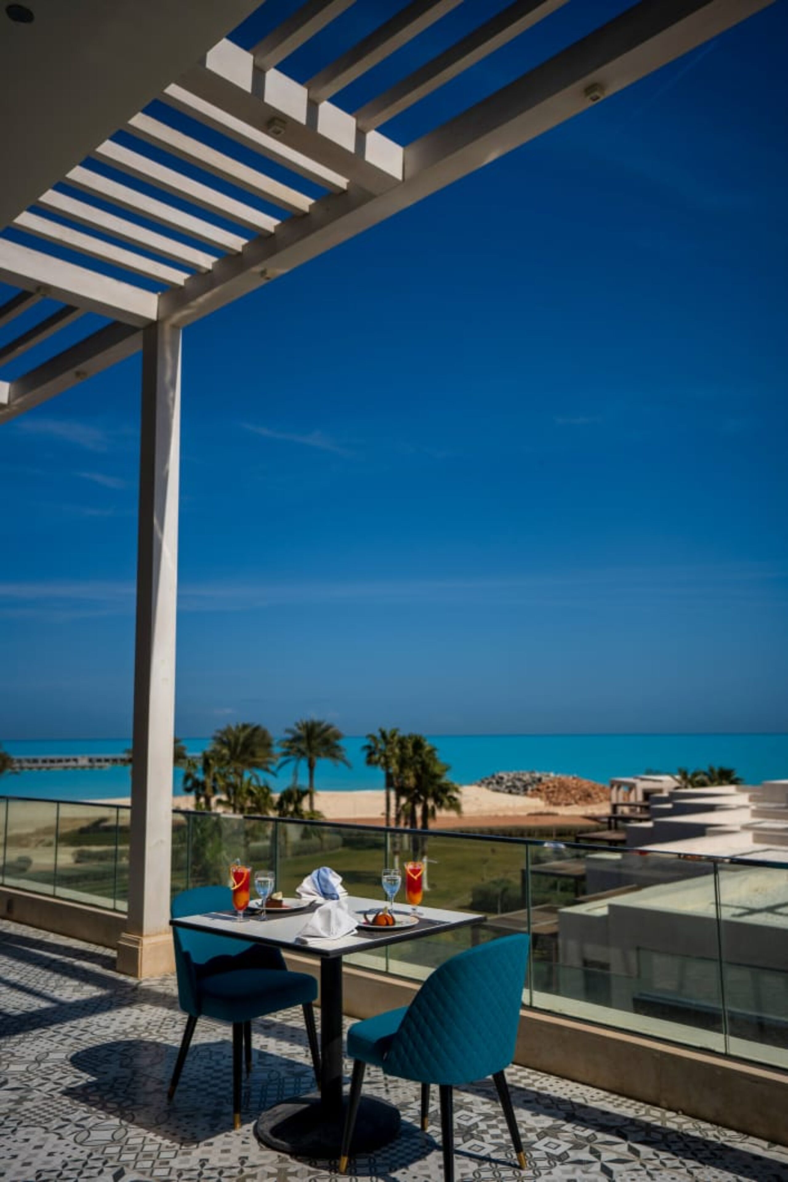 A balcony with a table and chairs, overlooking a beach and the ocean.