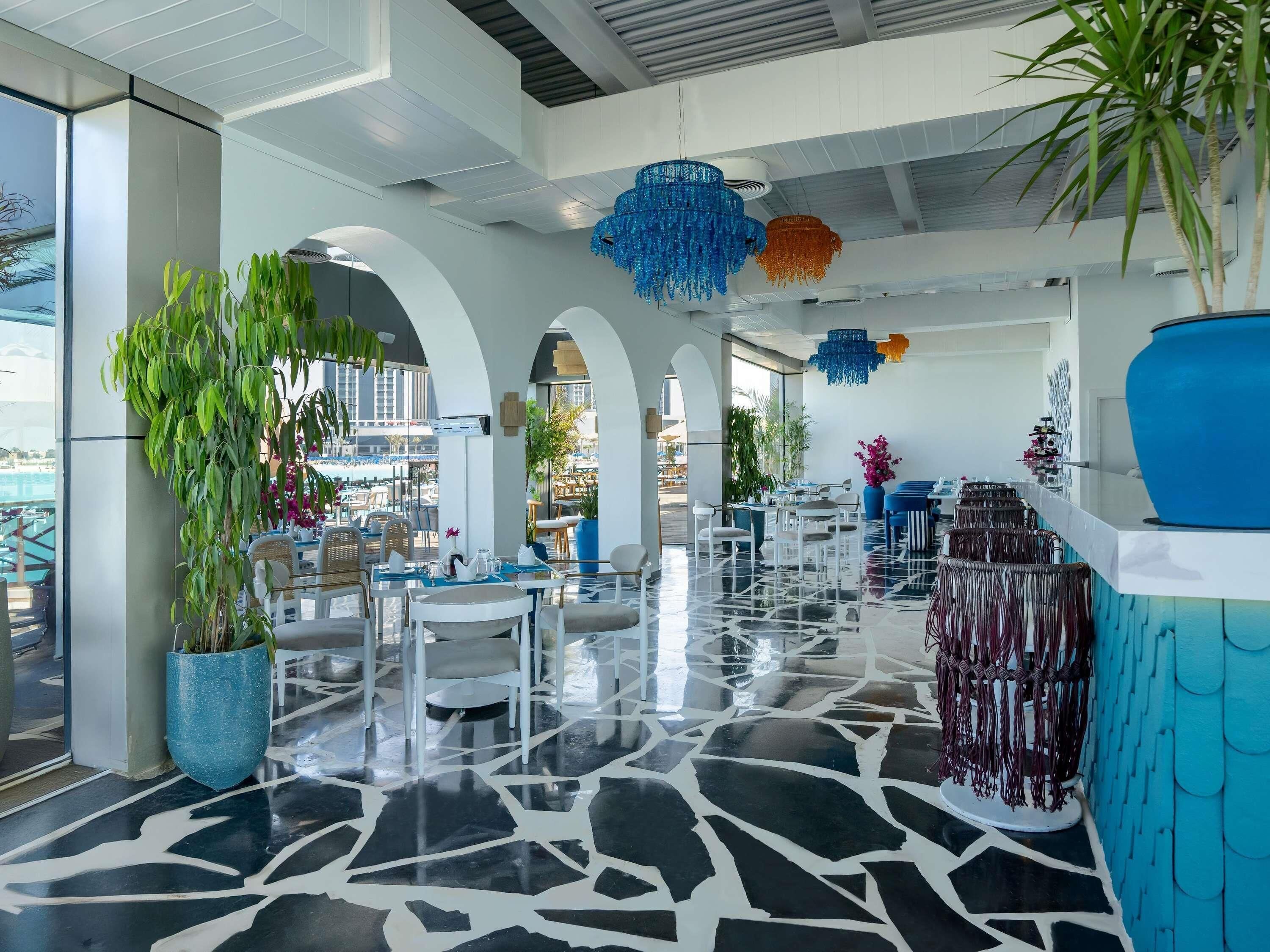 A modern hotel lobby with a terrazzo floor, white furniture, and blue and orange chandeliers.