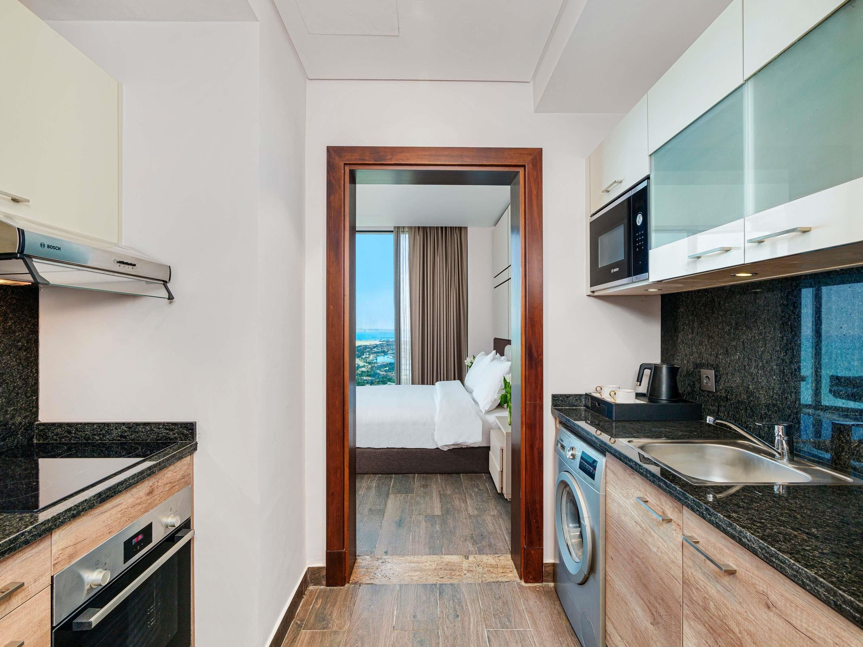 Una habitación de hotel compacta con kitchenette, lavadora y cama con vista a la ciudad.