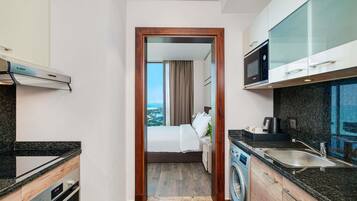 Une chambre d’hôtel compacte dotée d’une kitchenette, d’un lave-linge et d’un lit offrant une vue sur la ville.