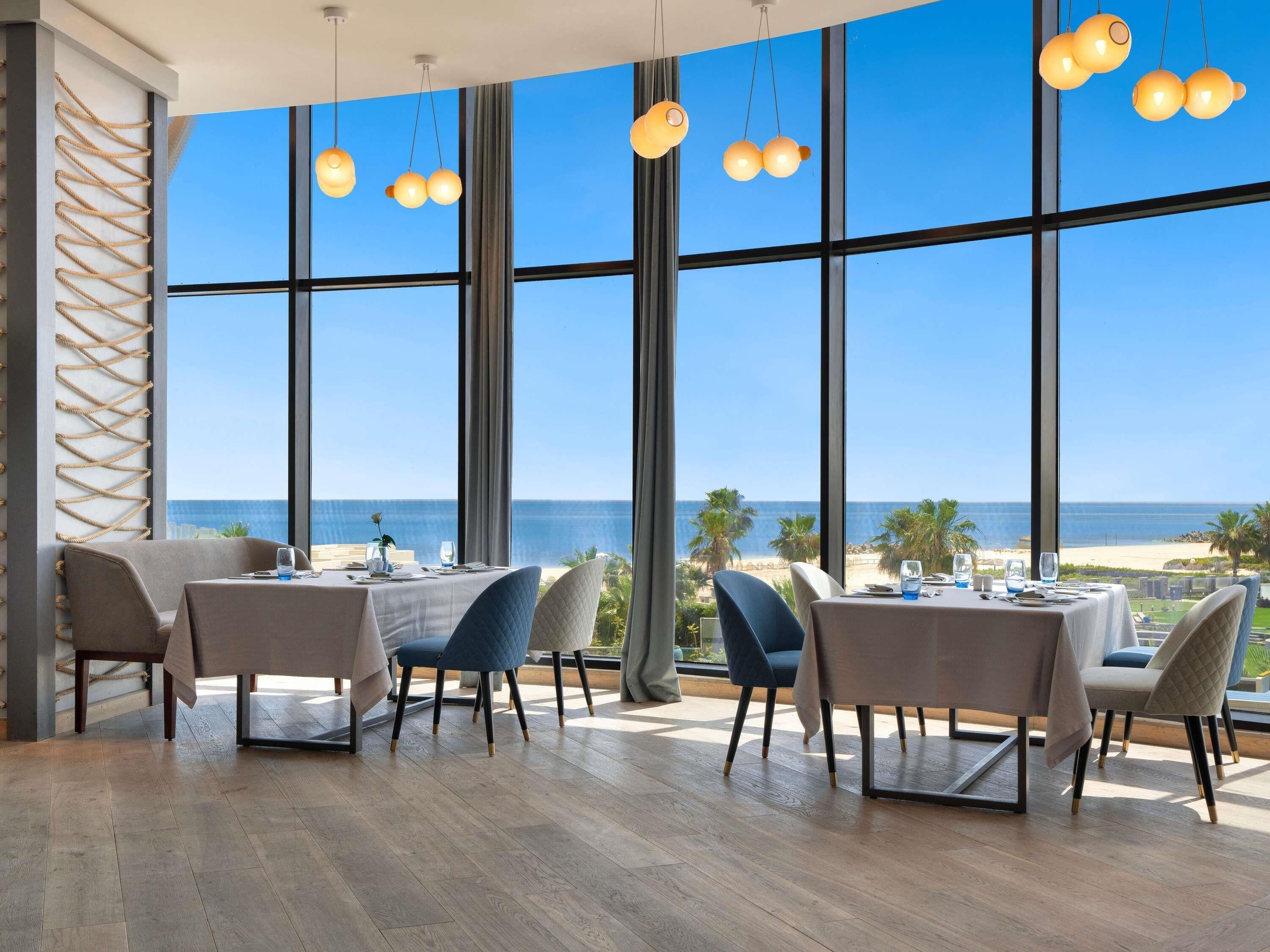 A dining area with large windows, a view of the beach, and hanging pendant lights.