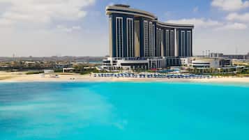 Un hotel de altura con fachada curva, una playa con sombrillas y aguas azules cristalinas.