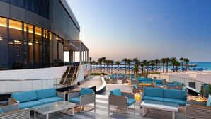 Un salón en la azotea con asientos exteriores, una escalera que lleva a un nivel superior y vistas a la playa y al océano.
