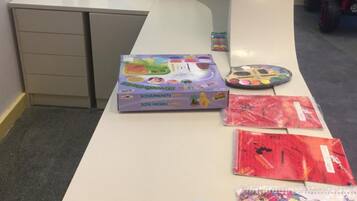 A desk with a box of Schaumkiste coloring books, a remote control, and several coloring books.