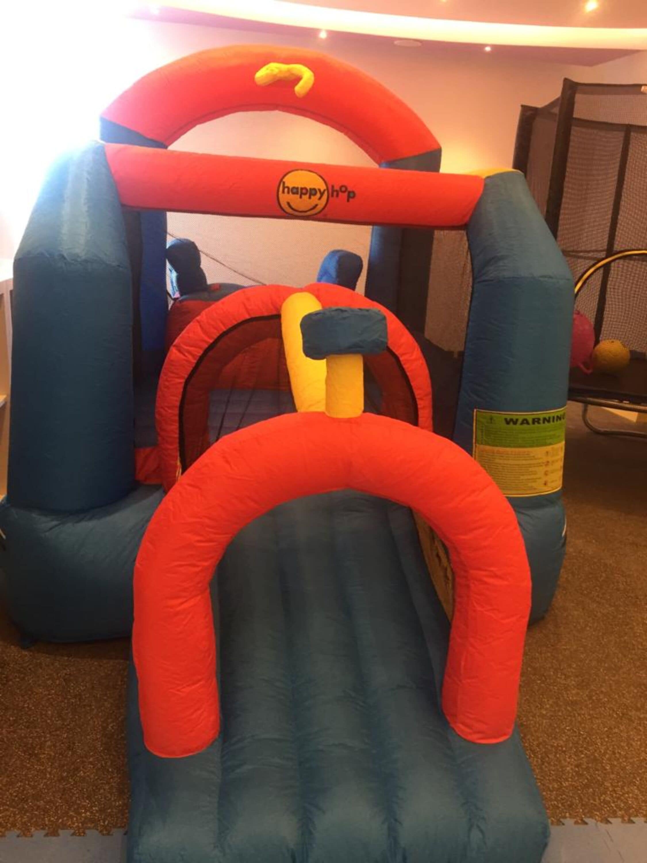 A blue inflatable bouncy castle with a red slide and a 'happy hop' logo.