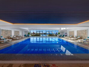 A large indoor swimming pool with lounge chairs and a view of the outside. - Rixos Premium Alamein (El Alamein)