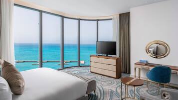 A hotel room with a large bed, a desk with a TV, and a view of the ocean.