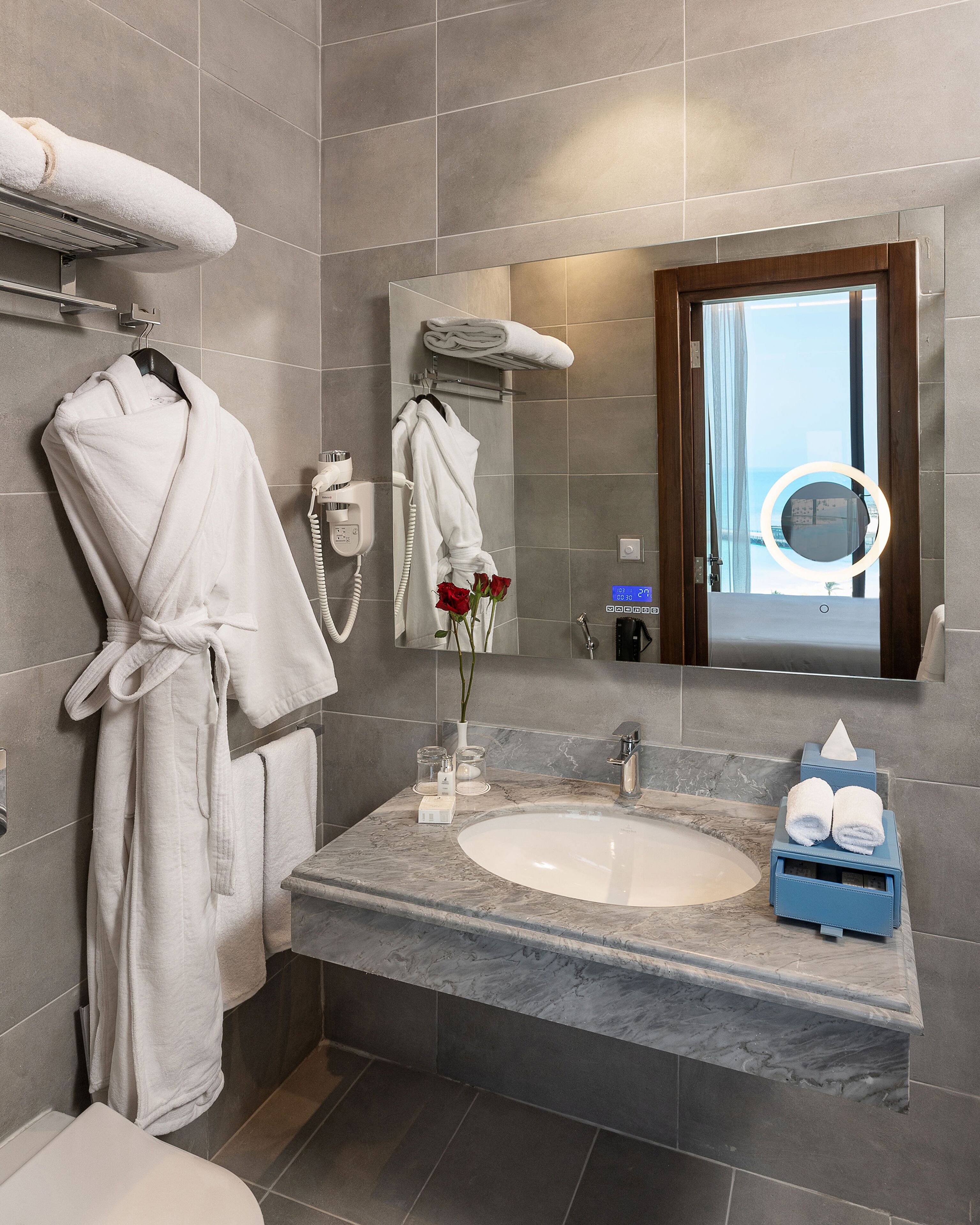 Une salle de bain moderne avec un lavabo en marbre, un grand miroir et un peignoir suspendu à un porte-serviettes.