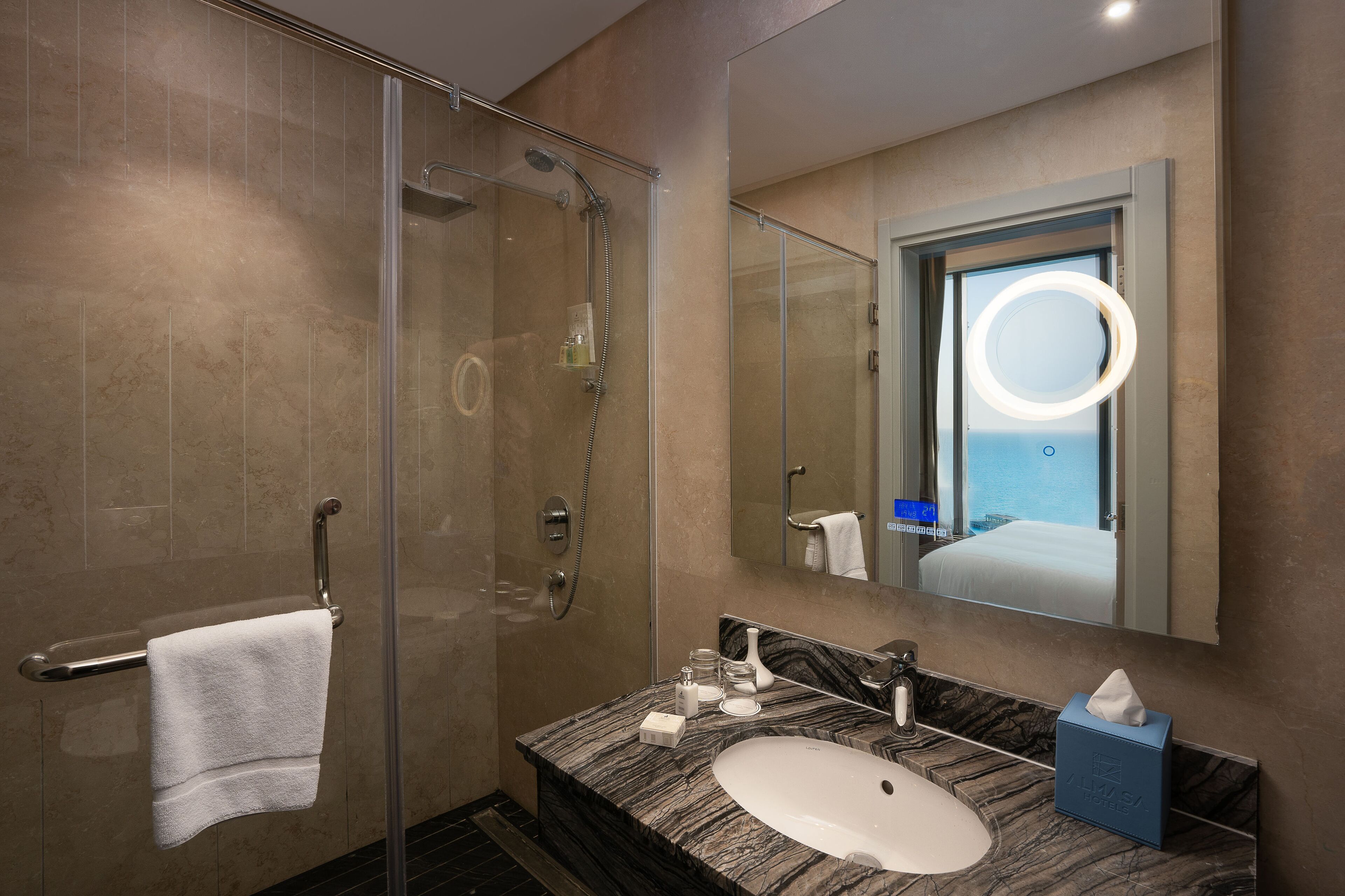 Ein modernes Badezimmer mit einer Glaskabine zur Dusche, einem мраморной Waschbecken und einem großen Spiegel, der einen Raum mit Meerblick reflektiert.