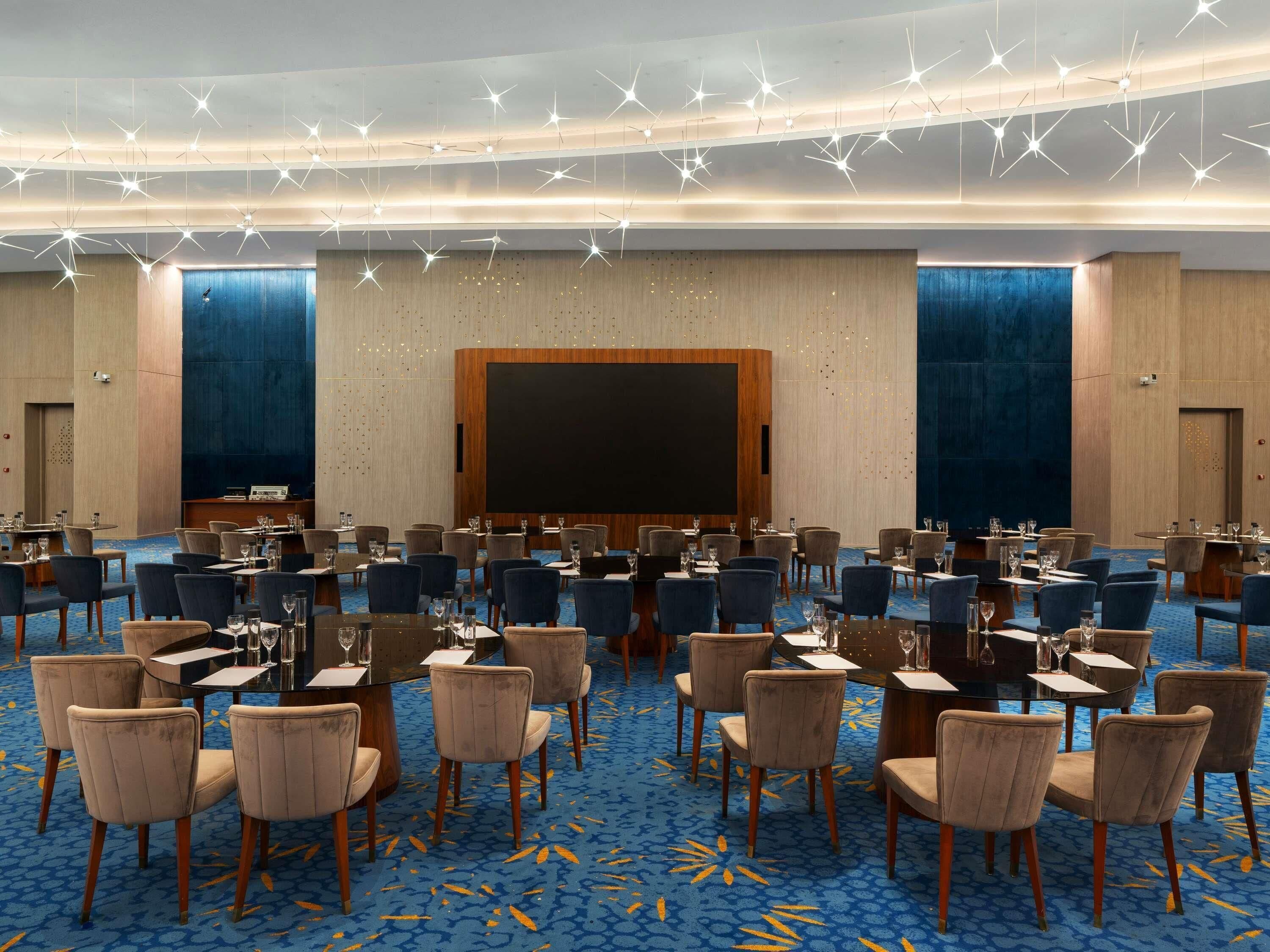 A conference room with multiple tables and chairs, a large screen, and star-shaped ceiling lights.