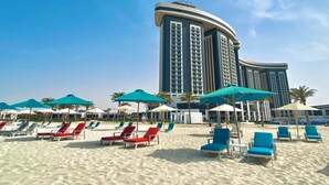 Una playa con hileras de tumbonas y sombrillas, y un gran edificio de hotel al fondo.