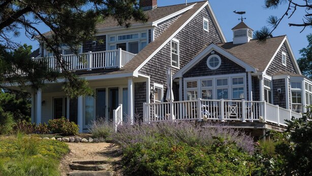 A two-story house with a balcony, a chimney, and a garden with various plants. - 600 Feet to Private Association Cape Cod Bay Beach (2266) (Eastham)