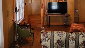 Un salón acogedor con televisor, un sofá estampado con motivos florales, una escalera de madera y un ventilador de techo.