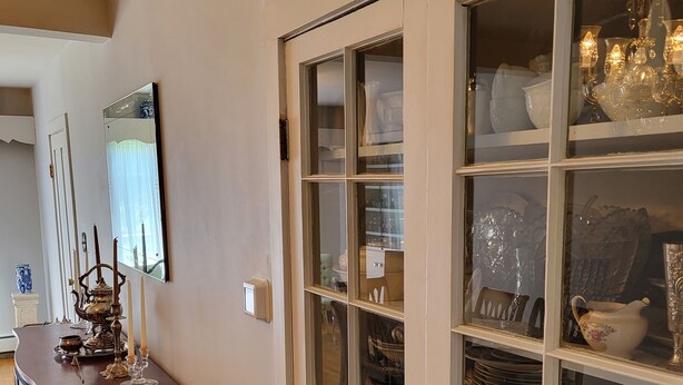 Una habitación con un escritorio de madera, una silla, un espejo y un aparador de vidrio con vajilla.