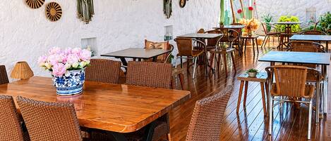 Un restaurante con mesas de madera, sillas de mimbre, un tejado de paja y adornos colgantes en las paredes.