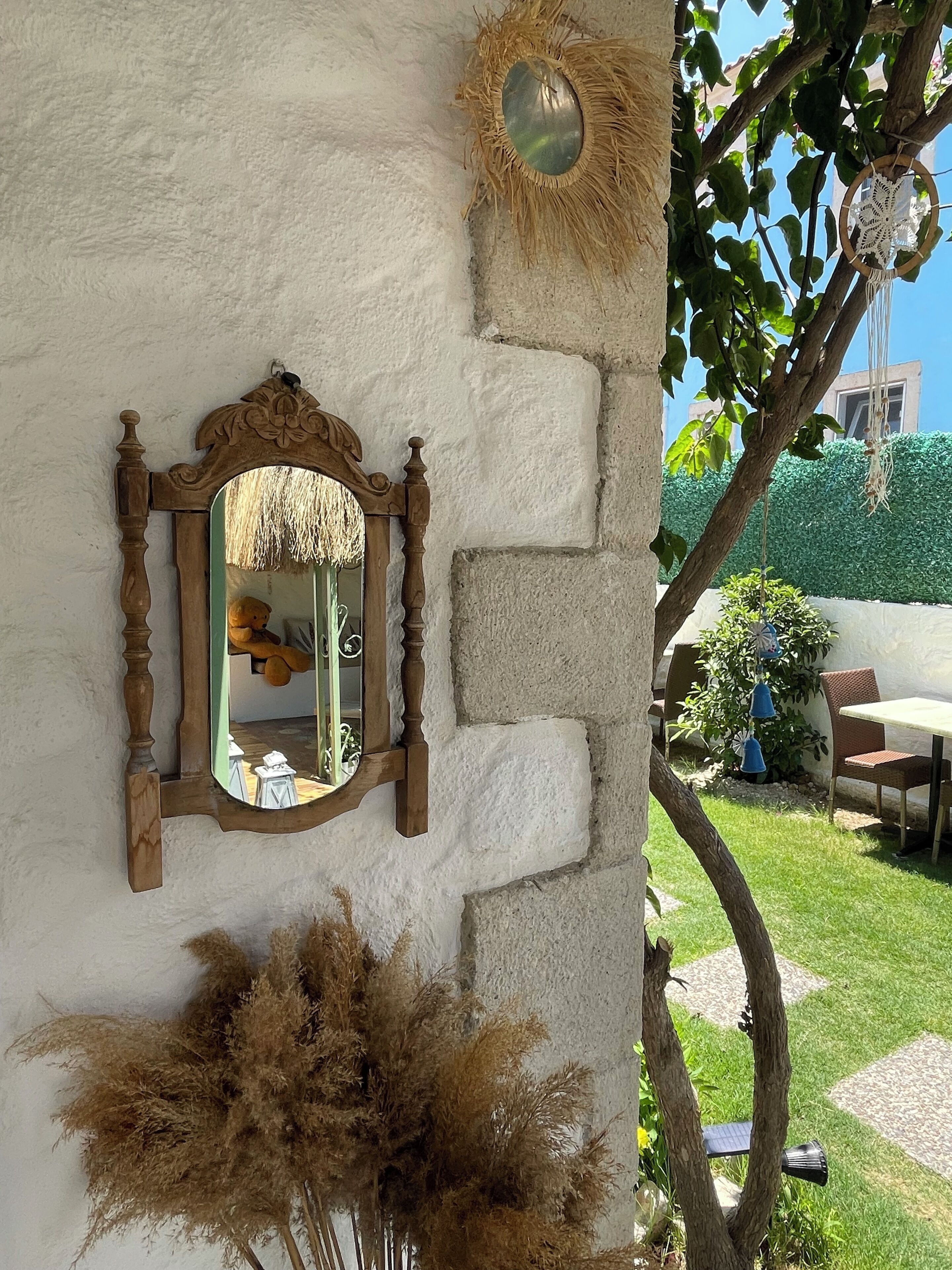 Un mur de pierres apparentes, agrémenté d’un miroir encadré en bois, d’un panier tressé et de plantes séchées.