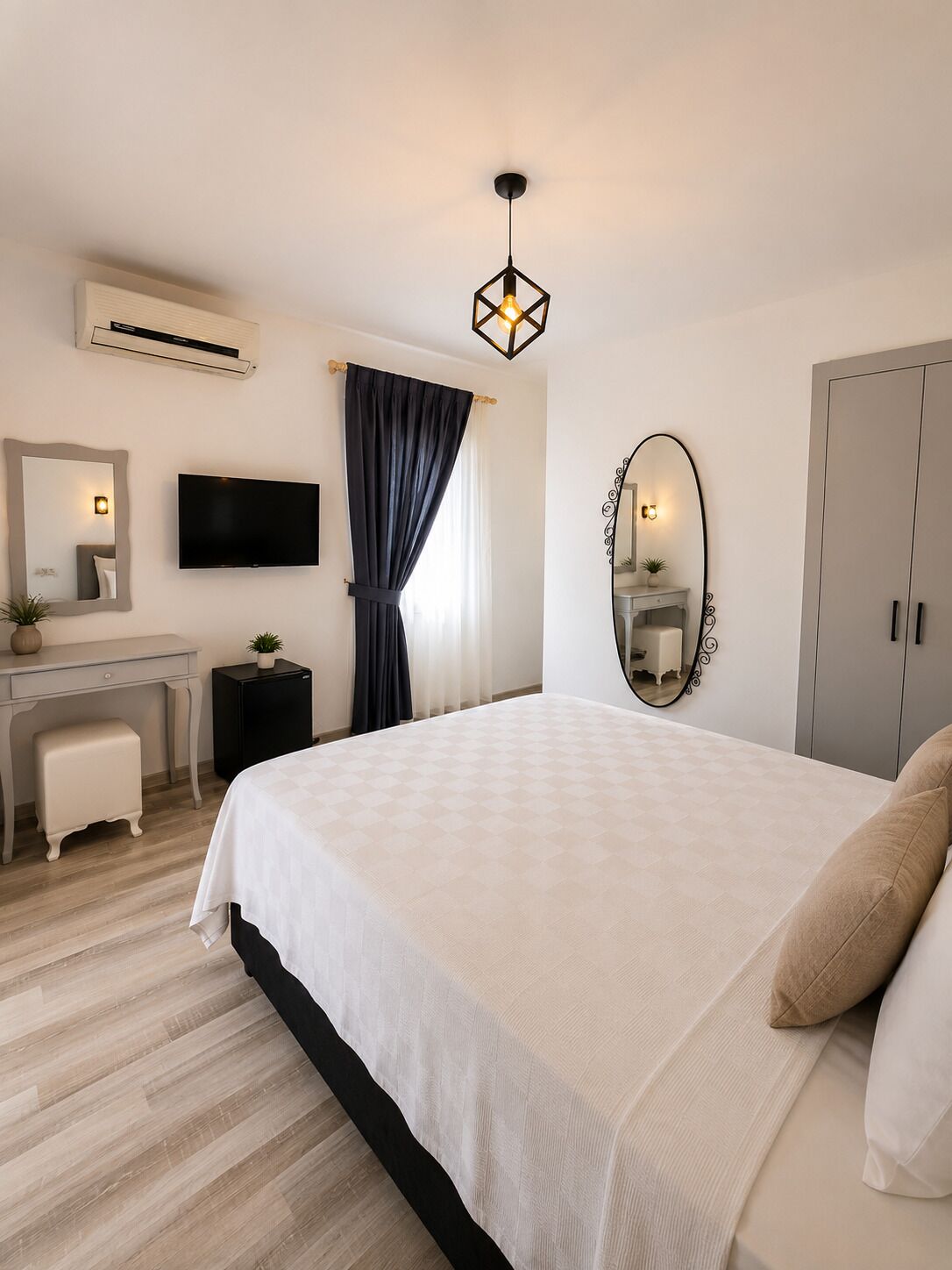 A bedroom with a bed, a desk, a TV, an air conditioner, a mirror, and a wardrobe.