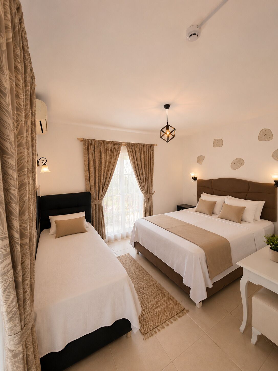 Une chambre d’hôtel avec deux lits, une table de chevet, une lampe de chevet, une fenêtre avec des rideaux, un luminaire fixé au mur et un plafonnier.