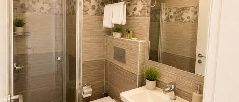 A modern bathroom with a glass shower enclosure, a toilet, a sink with a mirror, and a towel rack.