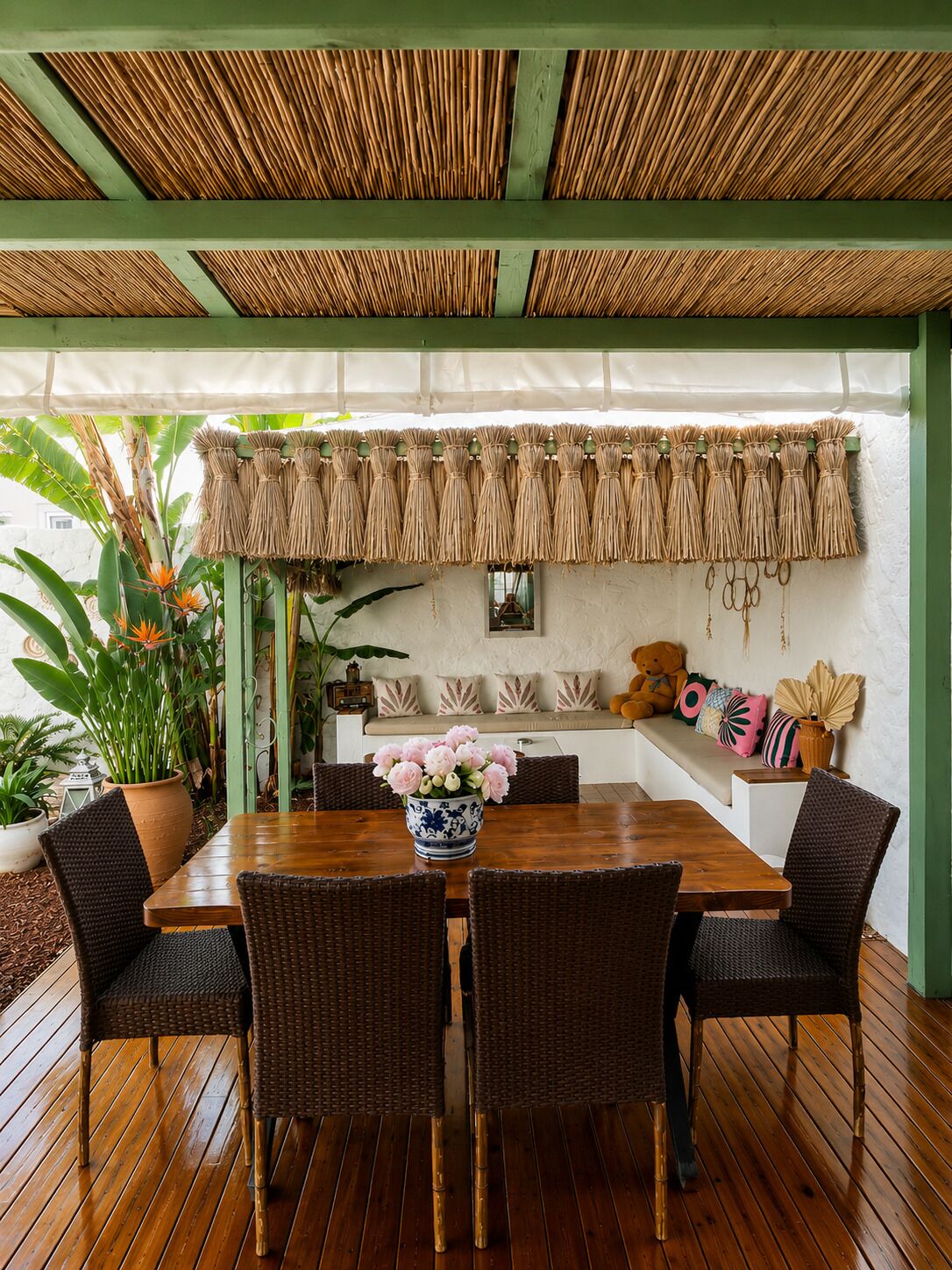A wooden deck with a table and chairs, surrounded by potted plants and a green wall.