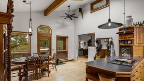 Une cuisine spacieuse avec des meubles en bois, un coin repas doté d’une grande table et de chaises, et une vue sur l’extérieur grâce à de nombreuses fenêtres.