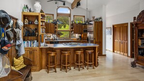 Une cuisine spacieuse avec des meubles en bois, un grand îlot central doté de tabourets de bar et une vue sur un paysage verdoyant par les fenêtres.