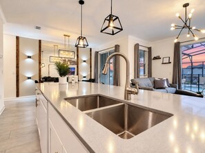 A modern kitchen with a central island, stainless steel sinks, pendant lighting, and a view of the outdoors. - Sunny Family Escape/ Private Pool & Themed Rooms (Kissimmee)