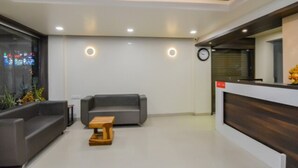 A modern reception area with a reception desk, two sofas, a small wooden table, and a clock on the wall. - Hotel Popular (Pune)