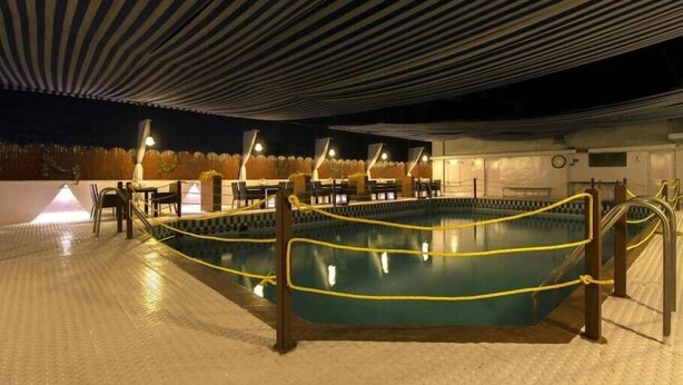 A pool area with a checkered pool edge, a covered seating area, and a clock on the wall. - Hotel Popular (Pune)