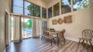 Un espace repas avec une table et des chaises en bois, de grandes fenêtres et une vue sur une piscine.